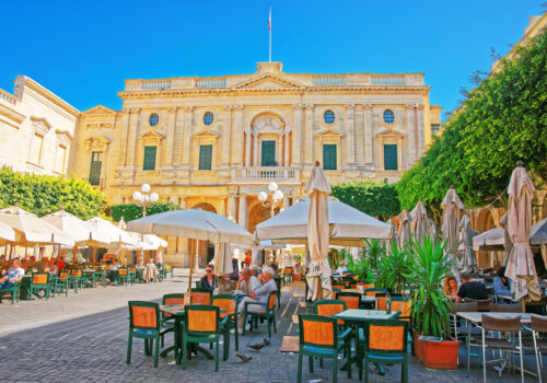 Valletta, Malta - April 1, 2014: People resting at open air cafes at Republic Square with National Library in Valletta old town, Malta